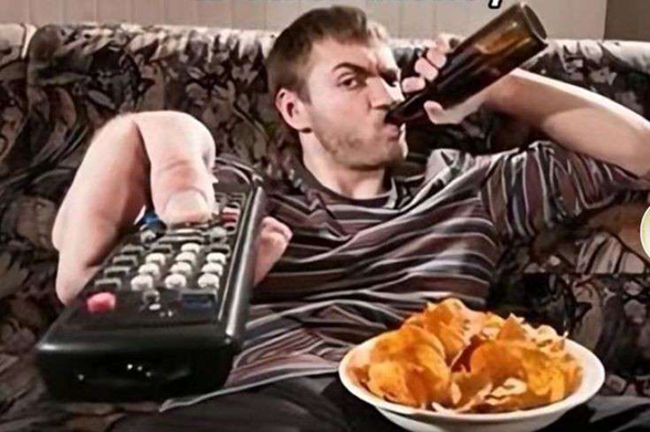 Guy sitting on a couch drinking beer and holding a TV remote